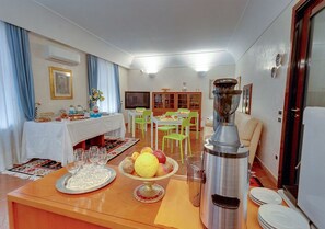 Un comedor con una mesa preparada para cuatro personas, un frutero y una cafetera.