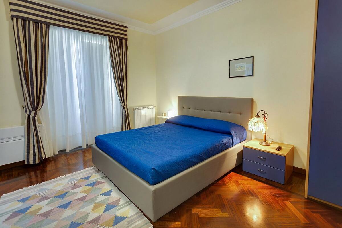 A bedroom with a bed, nightstand, lamp, and curtains.