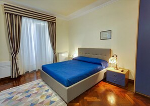 Un dormitorio con cama, mesita de noche, lámpara y cortinas.