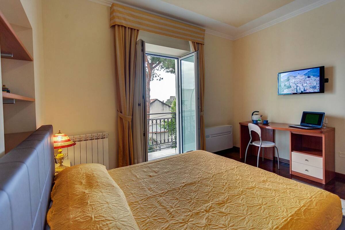 A hotel room with a bed, a desk, a chair, a TV, and a window with curtains.