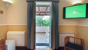 Une pièce dotée d’une porte-fenêtre coulissante donnant sur un balcon, d’un climatiseur blanc, d’une chaise en bois et d’un téléviseur fixé au mur.