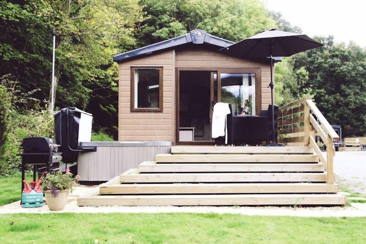 Eine kleine Holzhütte mit einer Terrasse, einem Grill und einem Sonnenschirm.