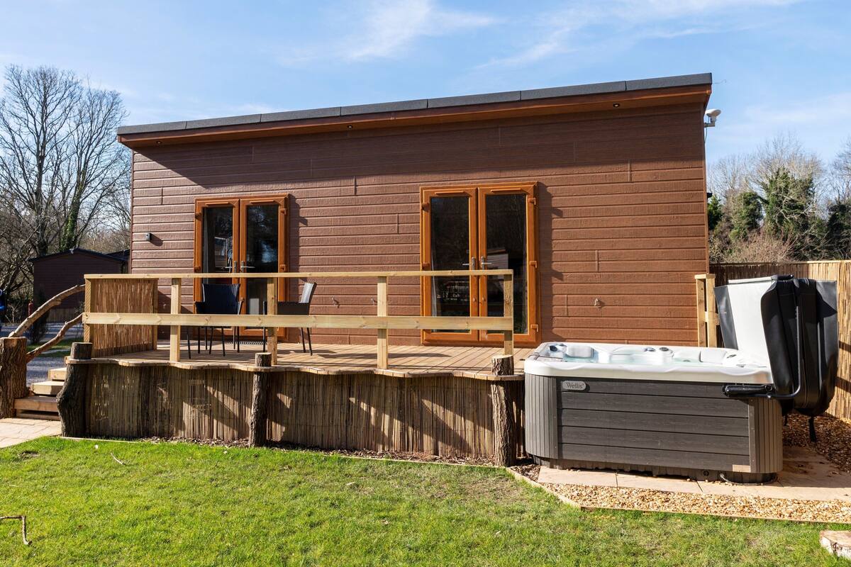 Eine Holzhütte mit einer Terrasse, zwei großen Fenstern und einem Whirlpool.