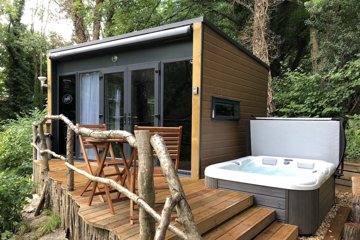 Eine Holzterrasse mit Whirlpool und einer kleinen Hütte mit Glastüren.