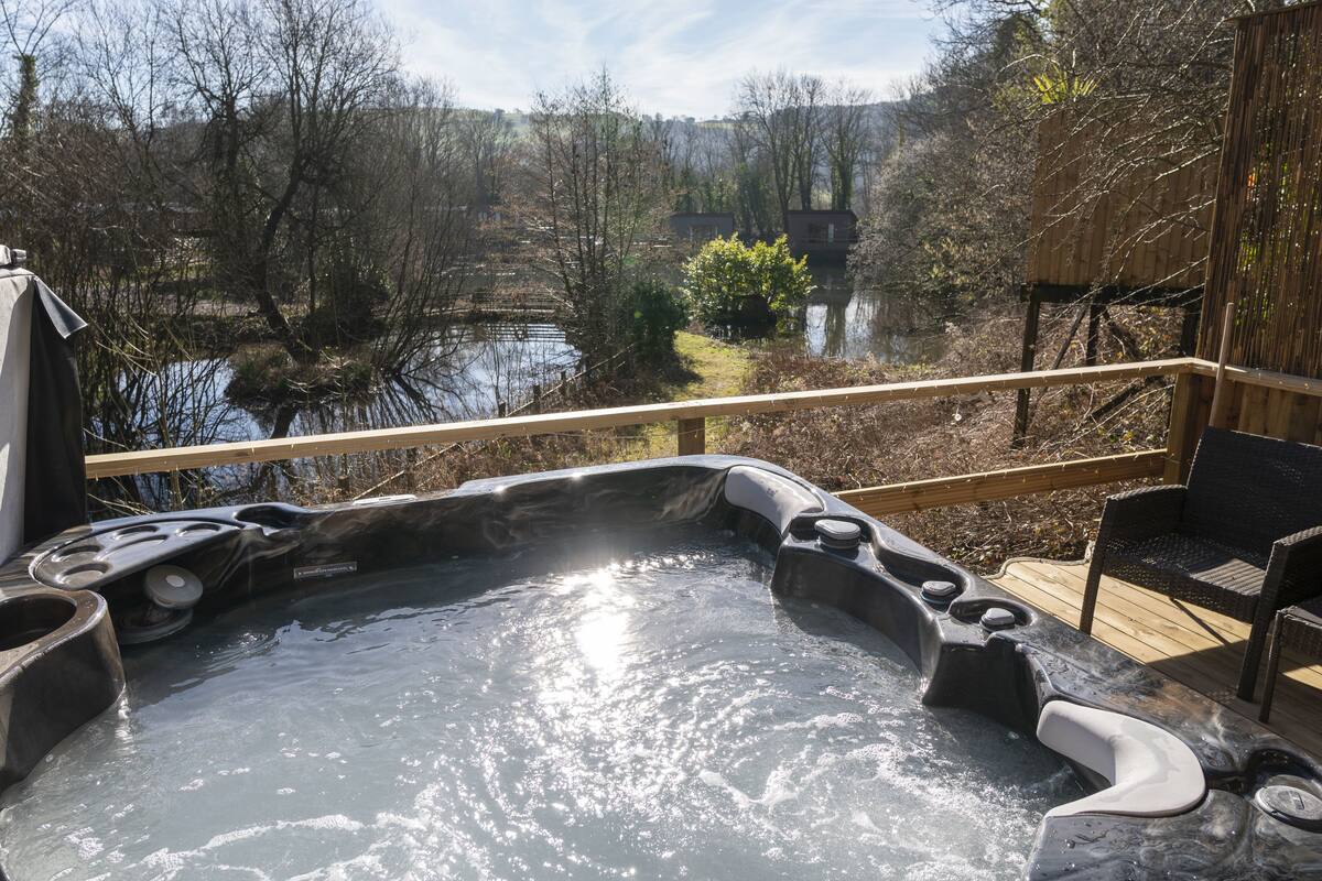 Ein Whirlpool mit einer Holzterrasse und Blick auf See und Bäume.