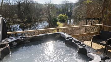 A hot tub with a wooden deck and a view of a lake and trees.