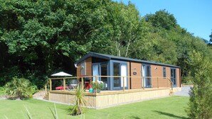 A wooden cabin with a deck, surrounded by lush greenery. - Herons Lake Retreat (Mold)