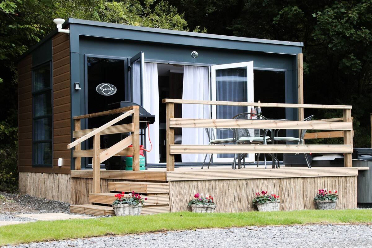 Eine kompakte, moderne Holzhütte mit einer Holzterrasse und einer Sitzgelegenheit im Freien.