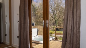 A room with a sliding glass door leading to an outdoor hot tub area. - Herons Lake Retreat (Mold)