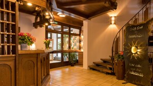 Un hall d’hôtel avec des boiseries, un comptoir d’accueil, des plantes en pot et un escalier.
