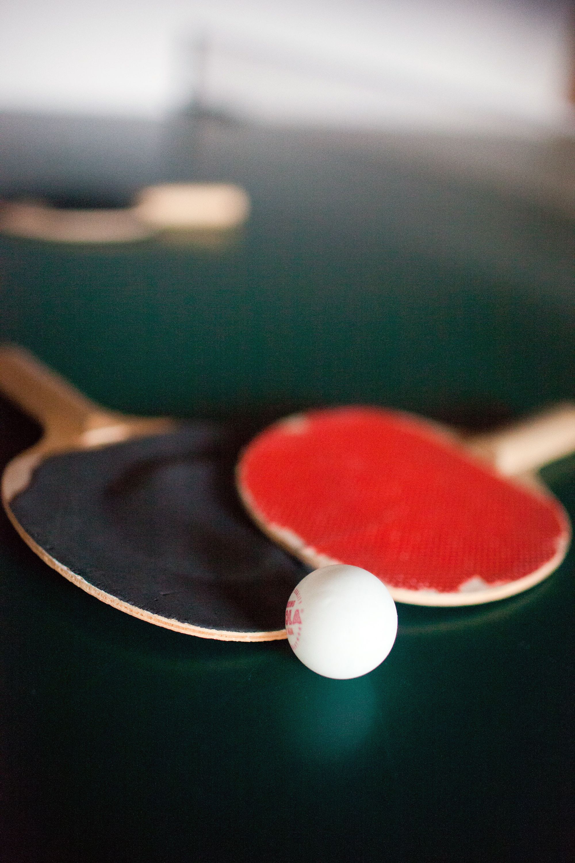 A close-up of two ping pong paddles and a ball on a dark surface.