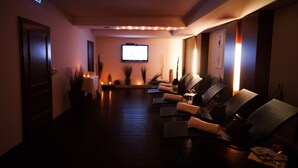 A dimly lit lounge area with reclining chairs, a flat-screen TV mounted on the wall, and a small table with a candle. - Sonnbichl (Lam)