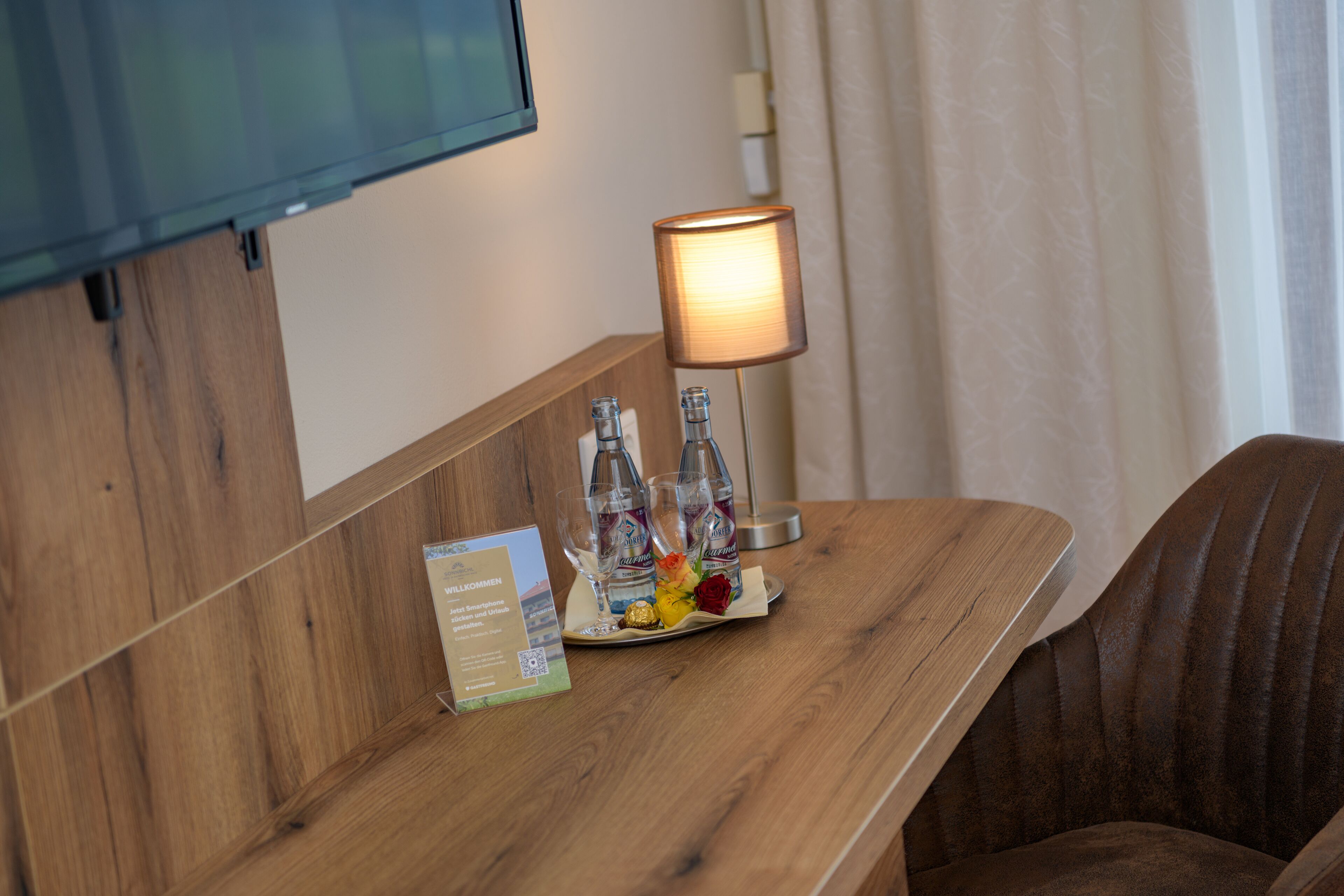 Een houten receptiebalie met een lamp, twee flessen en een dienblad met een bloem en een chocolade.