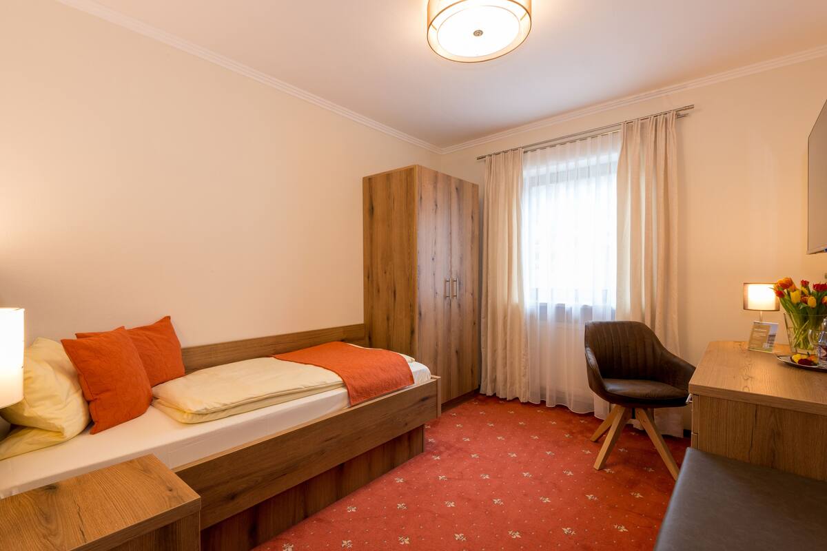 Une chambre d’hôtel avec un lit, un bureau, une chaise et une fenêtre avec des rideaux.