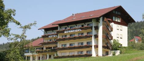 Un hotel de varios pisos con balcones, un techo rojo y un letrero que dice 'HOTEL SONNABACH'.