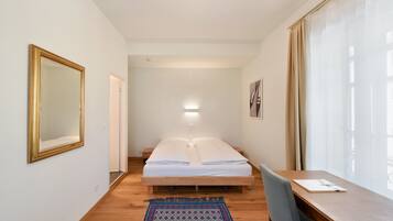 Ein Schlafzimmer mit einem Bett, einem Schreibtisch, einem Stuhl, einem Spiegel und einem Fenster mit Vorhängen.