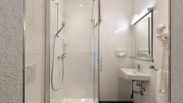 Un baño moderno con ducha envuelta en cristal, un lavamanos blanco y un espejo con toallero.