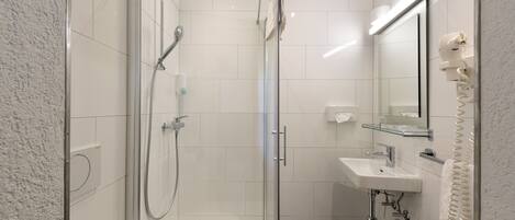 A modern bathroom with a glass-enclosed shower, a white sink, and a mirror with a towel rack.