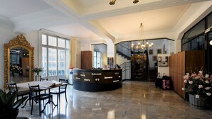 A hotel reception area with a curved desk, a large mirror, and a chandelier. - Hotel National Bern (Bern)
