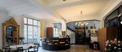A hotel reception area with a curved desk, a large mirror, and a chandelier.