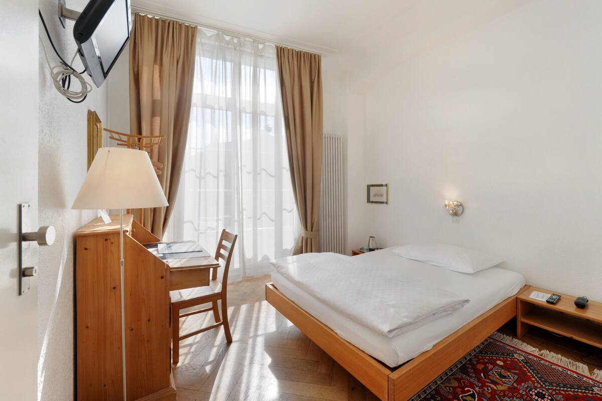 Une chambre d’hôtel avec un lit en bois, un bureau avec une lampe, une chaise et un téléviseur fixé au mur.