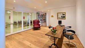 A conference room with a wooden table, black chairs, a red armchair, a bookshelf, and a painting on the wall. - Hotel National Bern (Bern)