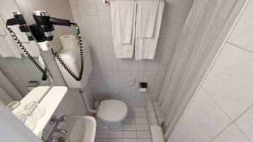 Un baño pequeño y moderno con inodoro, lavamanos y ducha. Hay toallas colgadas en la pared y un secador de pelo también allí.