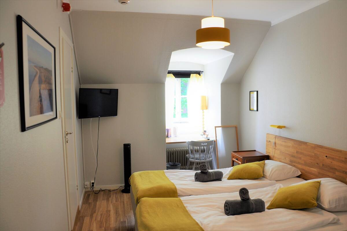 Ein Hotelzimmer mit zwei Betten, einem Fernseher, einem Fenster mit Vorhängen und einem Holzkopfende.