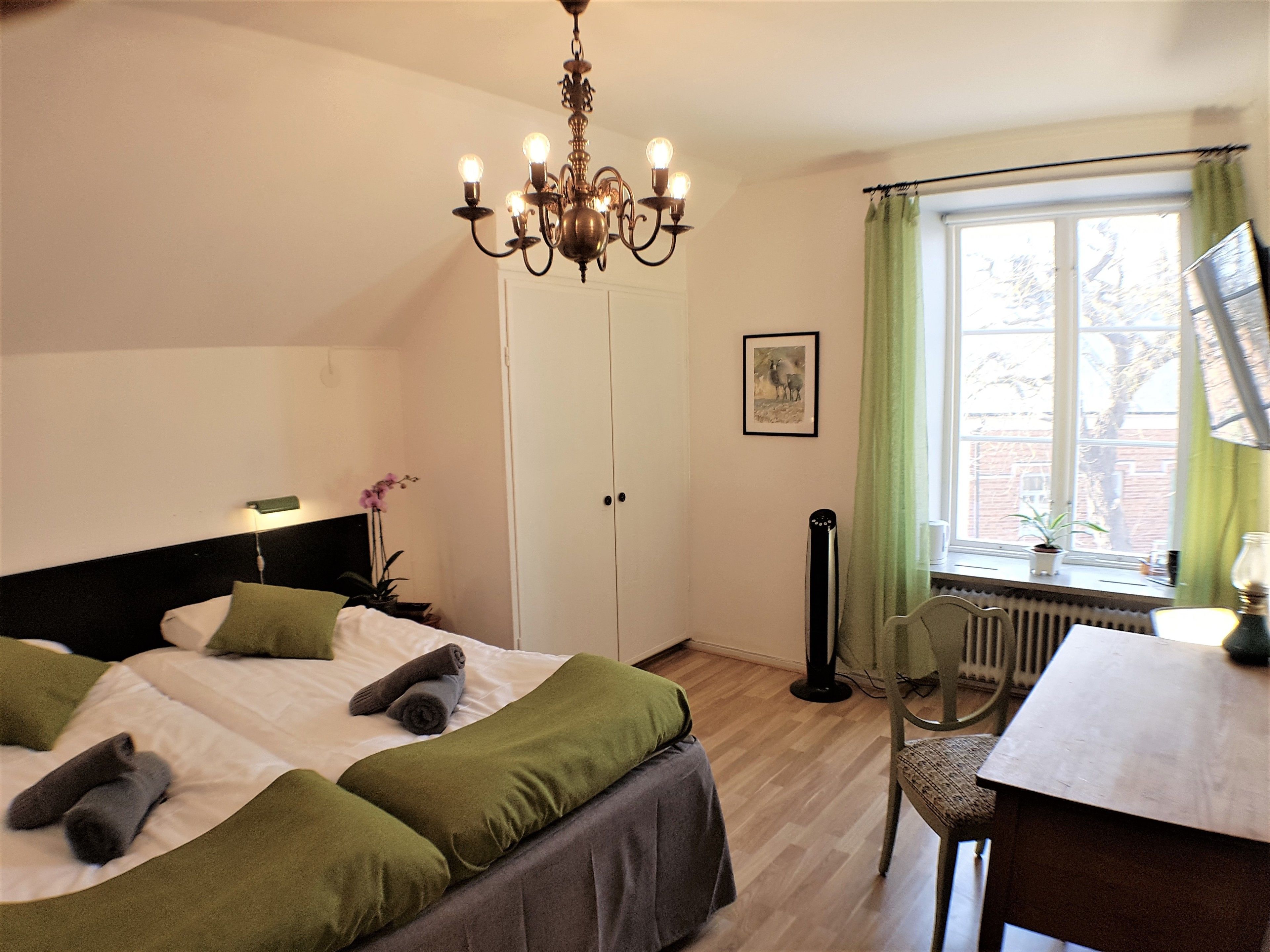 Un dormitorio con cama, escritorio, radiador y ventana con cortinas.