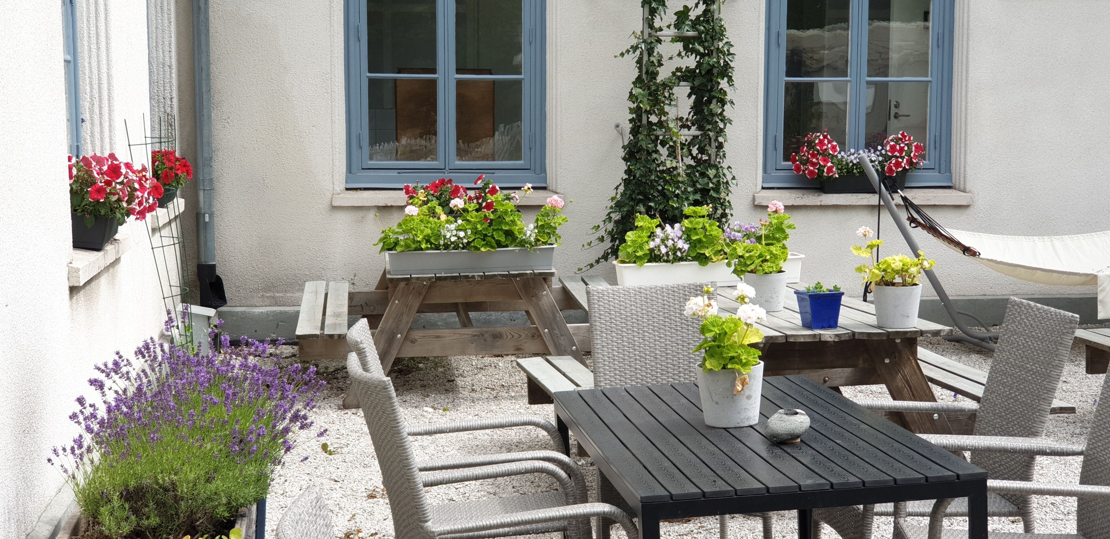 Un patio al aire libre con mobiliario de mimbre, una mesa de madera y plantas en macetas.