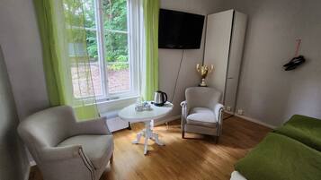A room with two armchairs, a small table with a kettle, a TV mounted on the wall, and a wardrobe.
