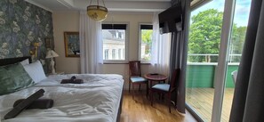 Un dormitorio con cama, una mesa con sillas, una ventana con cortinas y un balcón.