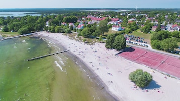 Vista aérea de una playa con un muelle, cancha de tenis y una zona residencial al fondo.