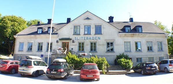 Un edificio con el letrero "SLITEBADEN" en la fachada. Hay varios coches estacionados adelante y una escalera que conduce a la entrada.