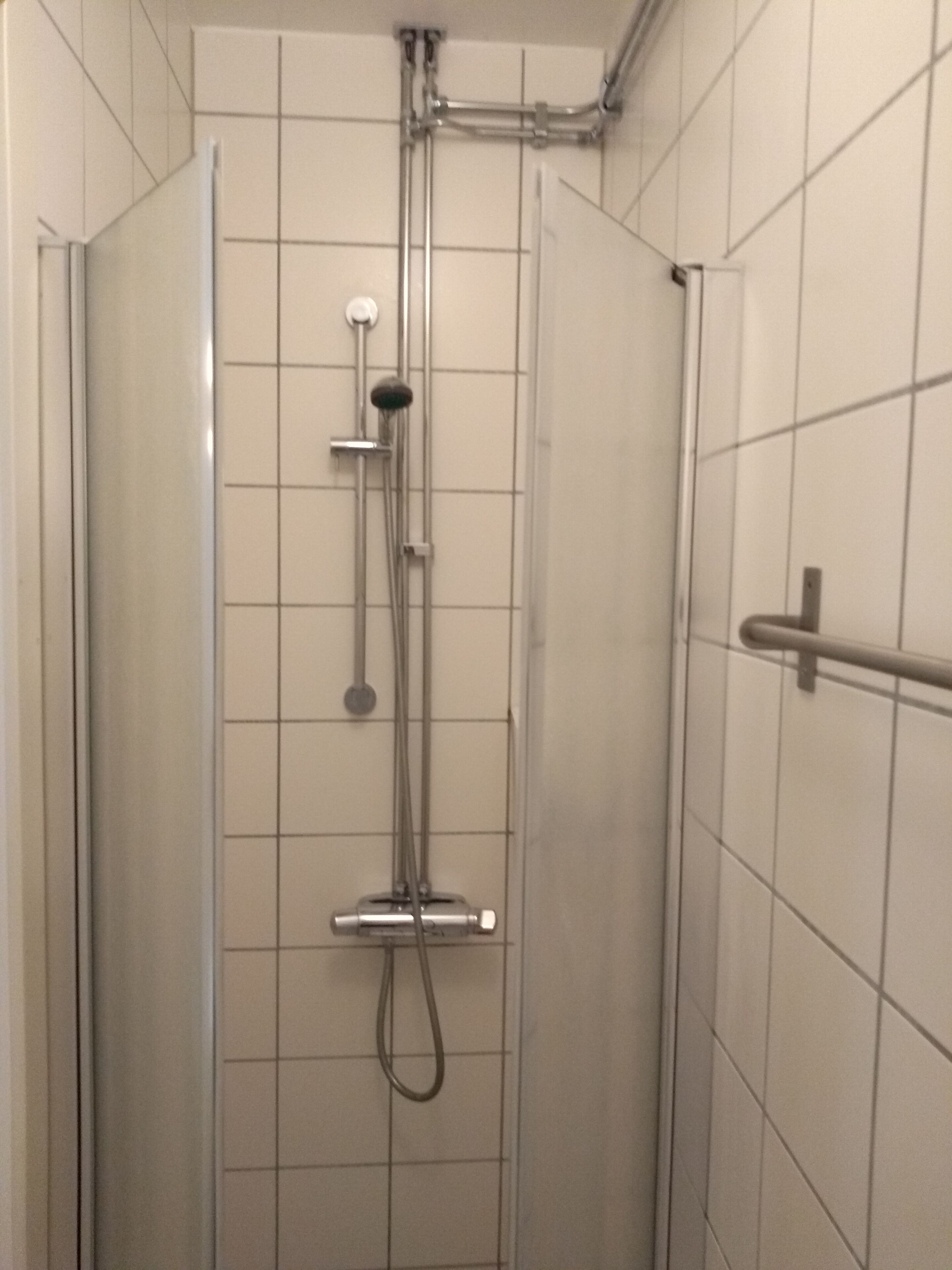 A shower with a handheld showerhead, a wall-mounted faucet, and a handheld showerhead.