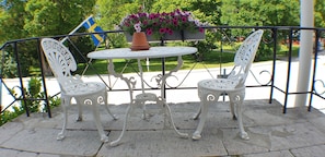Una mesa de metal blanco y dos sillas en un patio de piedra, con una maceta y una bandera sueca al fondo.