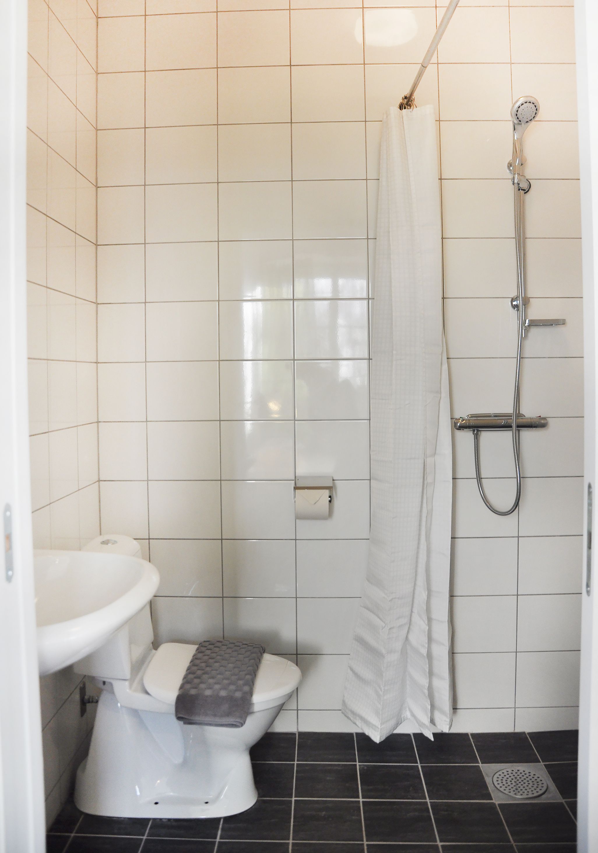 A small, tiled bathroom with a toilet, sink, and shower.