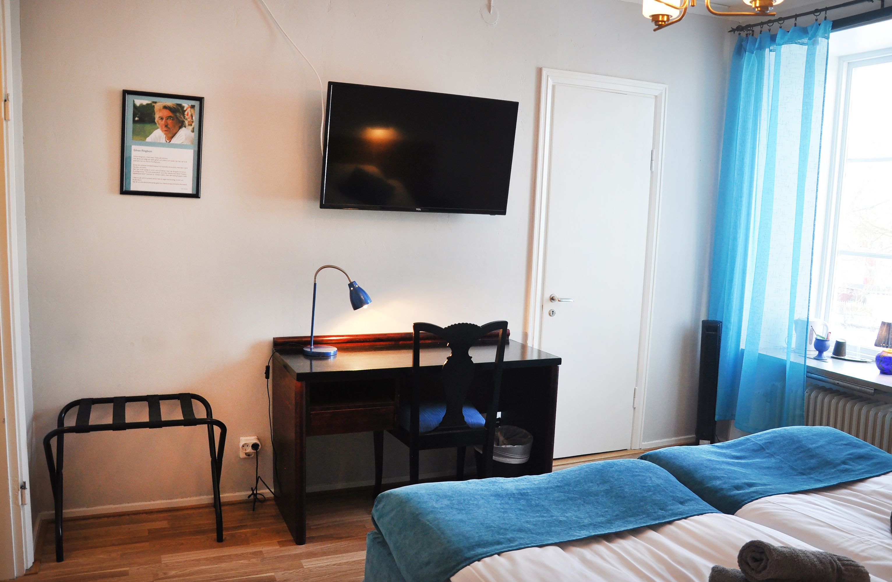 Un dormitorio con cama, escritorio, silla, televisor y ventana con cortinas.
