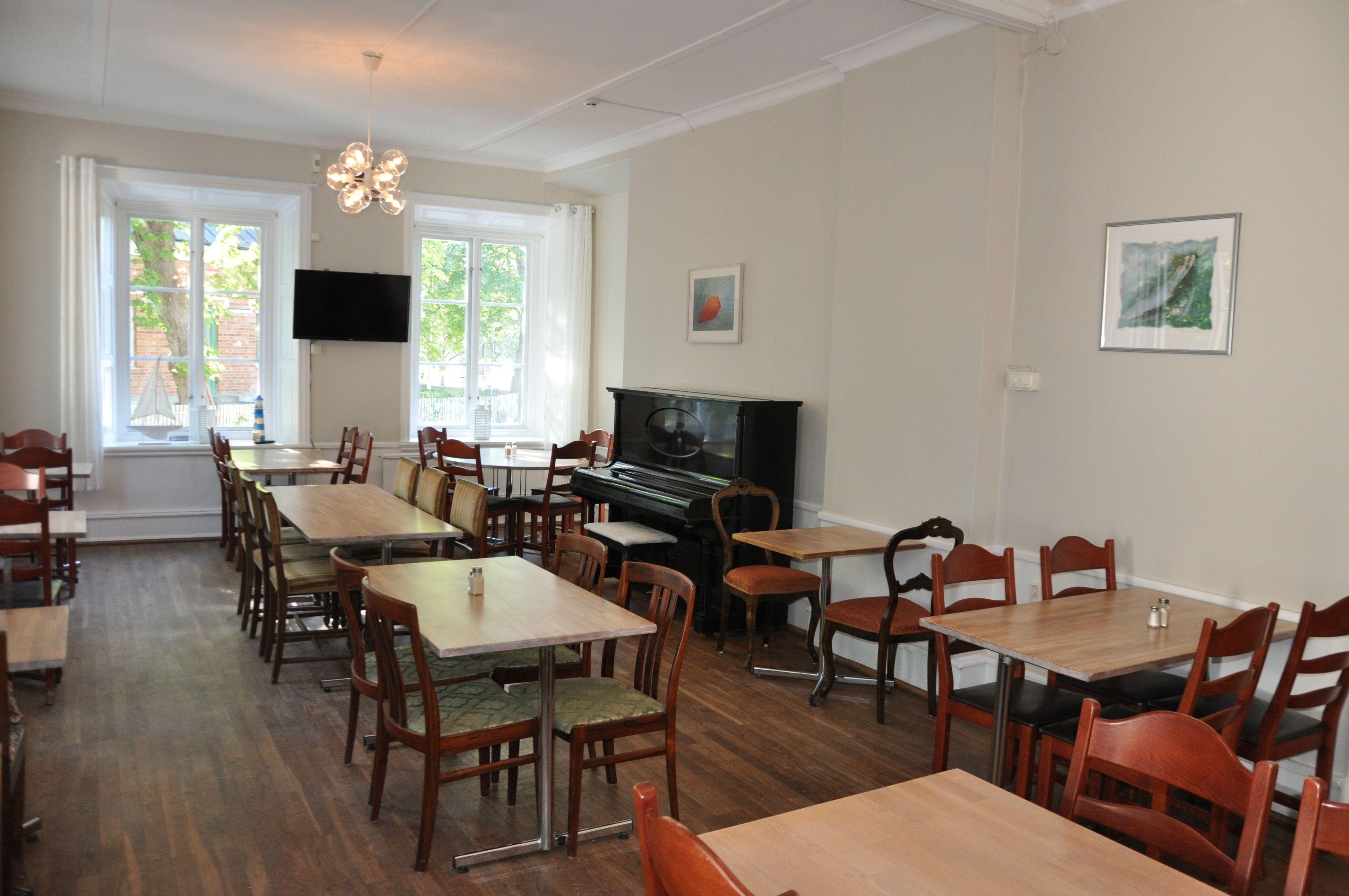 A dining area with multiple tables and chairs, a piano, and a television on the wall.