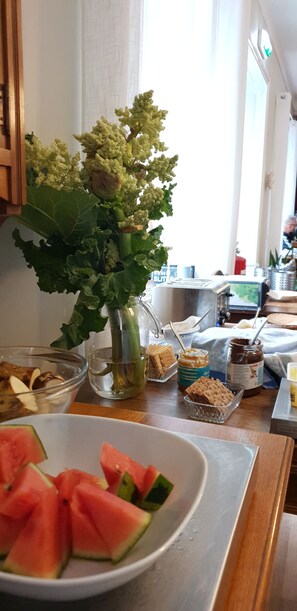 Una encimera de cocina con un bol de sandía cortada, un tarro de mantequilla de maní y un florero con plantas verdes.