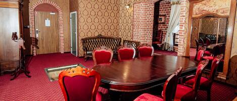 A conference room with a large round table, red upholstered chairs, a patterned wallpaper, and a brick wall.