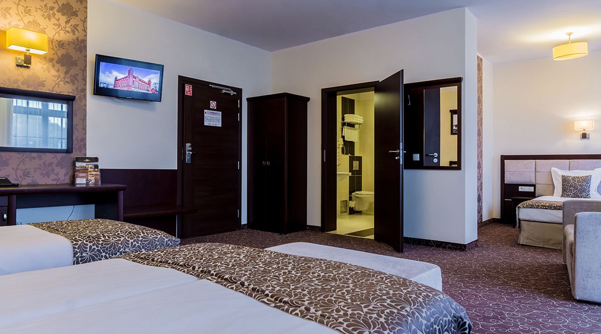 A hotel room with two beds, a desk, a television, a wardrobe, and a bathroom visible through an open door.
