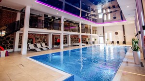A modern indoor swimming pool with a glass ceiling, multiple levels, and a stone wall design. - Zamek Gniew - Hotel Rycerski (Gniew)
