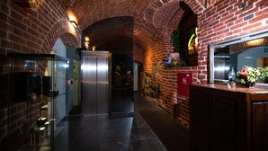 A narrow corridor with brick walls and a tiled floor, leading to a kitchen area with a refrigerator and a sink. - Zamek Gniew - Hotel Rycerski (Gniew)