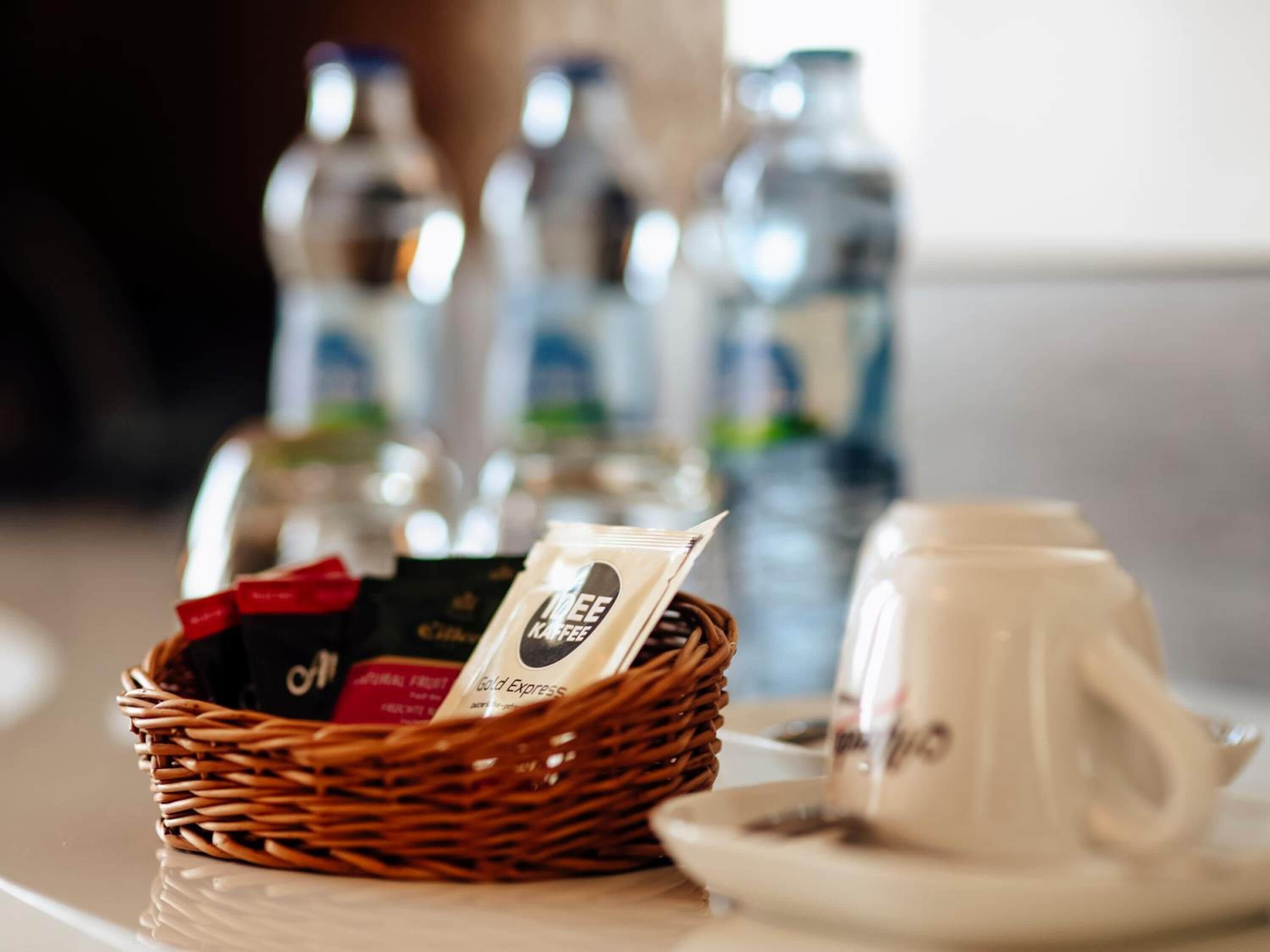 Un panier en osier contenant des sachets de café et une tasse, posés sur une table.
