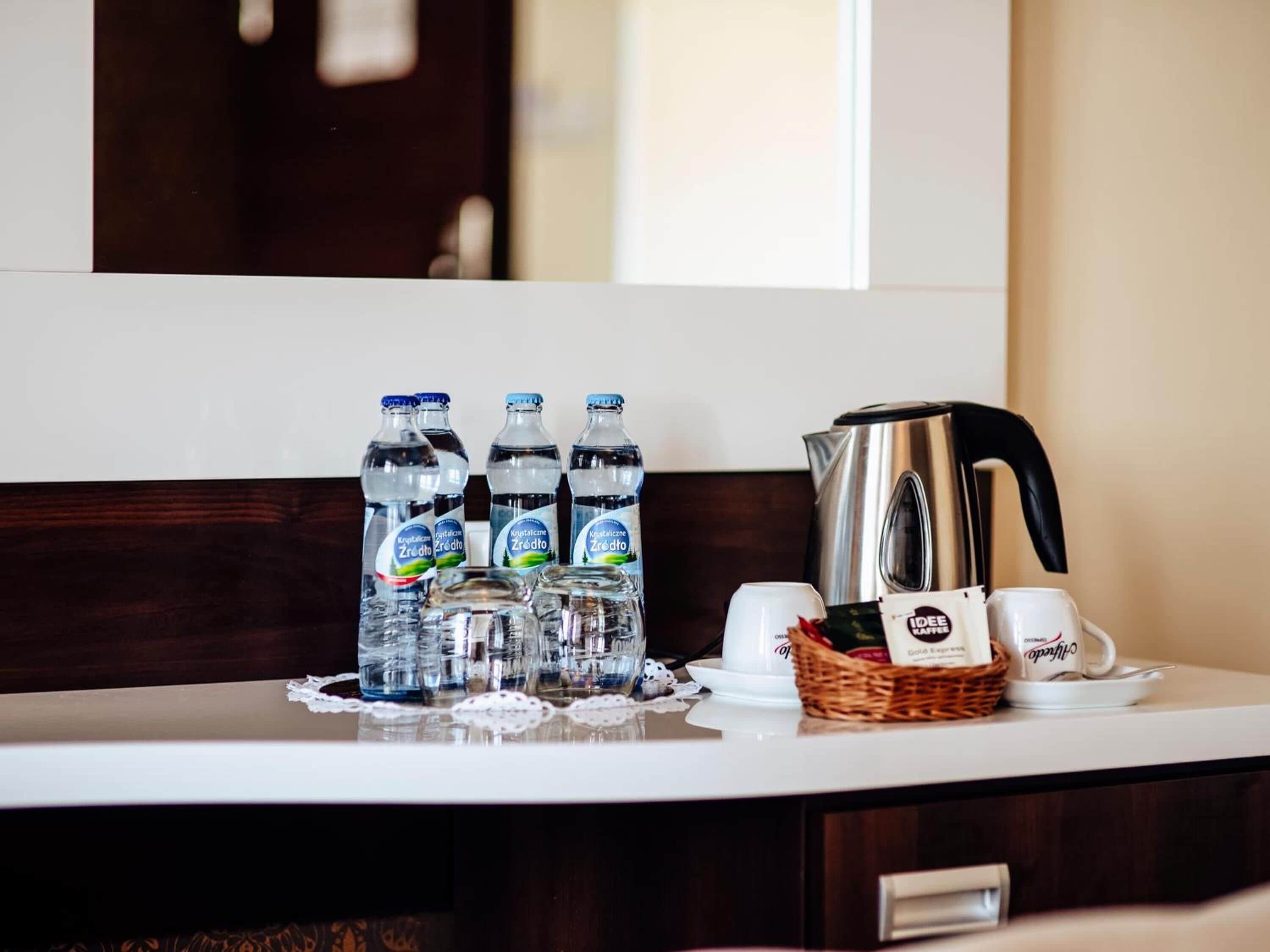 A hotel minibar with bottled water, coffee cups, and a kettle.