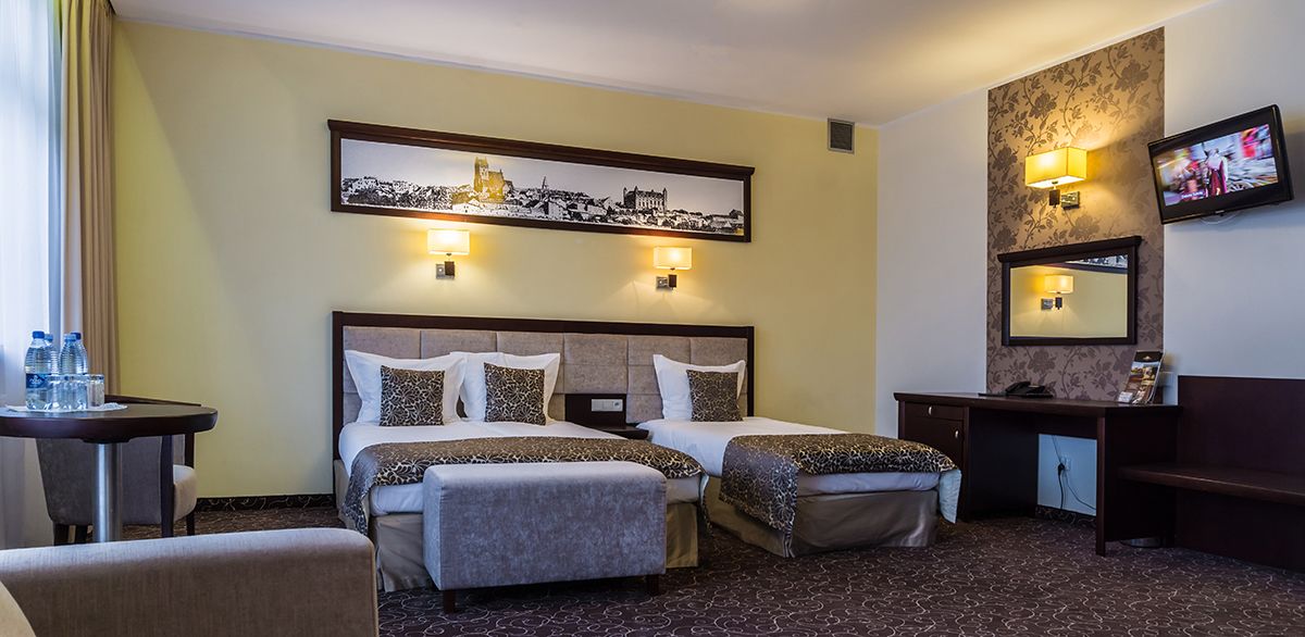 Habitación de hotel con dos camas, un escritorio, una silla, un televisor y un cuadro en la pared.