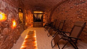 Una habitación con paredes de piedra, una chimenea, un banco y un área de estar con sillas.