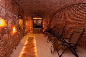 Um quarto com paredes de pedra, lareira, um banco e um espaço de estar com cadeiras.