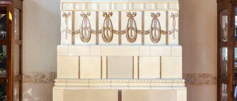 A fireplace with a decorative urn on top, surrounded by white tiles with gold accents.
